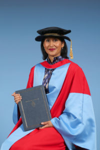 Dr Hayaatun Sillem seated in graduation regalia, holding her Honorary Degree