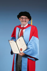 Professor Sir Ian Diamond, standing in graduation regalia, holding his Honorary Degree