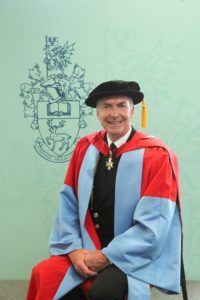 Admiral Dr Sir Tony Radakin, seated in graduation regalia in front of the University crest