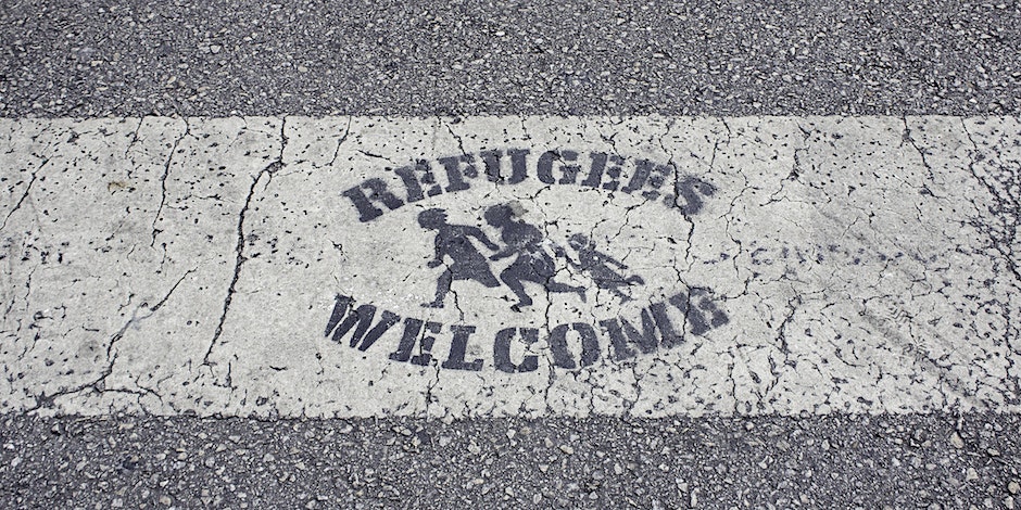 Refugess welcome message painted on tarmac with image of family fleeing